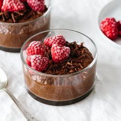 two bowls filled with chocolate and raspberries on top of a white tablecloth