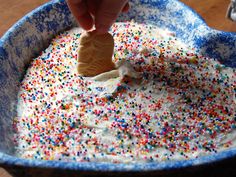 someone dipping a cookie into a bowl of sprinkles and white frosting