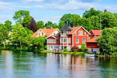 a red house sitting on the side of a lake next to trees and boats in the water