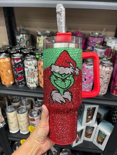 someone is holding up a red and green christmas tumbler in front of some cans