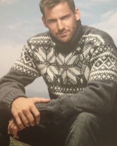 a man sitting on top of a grass covered field next to a sky filled with clouds