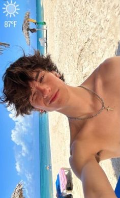 a young man standing on top of a sandy beach next to the ocean with his shirt off