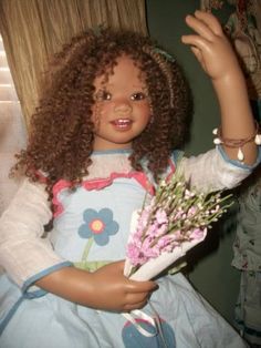 a doll with curly hair holding flowers in her hand