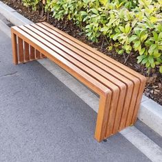 a wooden bench sitting on the side of a road next to bushes and shrubbery