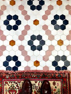 a pair of shoes sitting on top of a rug in front of a tiled wall