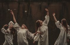 four women in white dresses are standing by the water with their arms up and hands raised