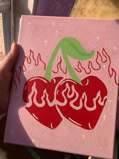 a person holding up a pink painting with two cherries on it's side