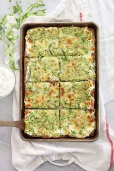 a casserole with broccoli and cheese in a pan next to a bowl of ranch dressing