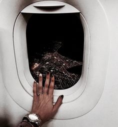 a woman's hand is on the edge of an airplane window as she looks at the city lights