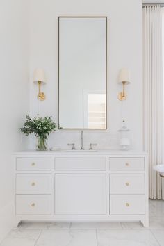 a white bathroom with two sinks and a large mirror above the sink, along with gold accents