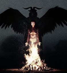 a woman with wings standing in front of a fire