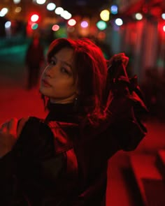 a woman standing on the street at night with her hand in her hair and looking off into the distance