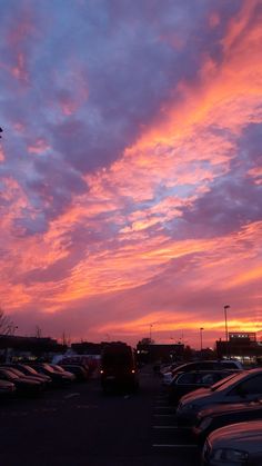 a parking lot filled with lots of parked cars under a pink and blue cloudy sky