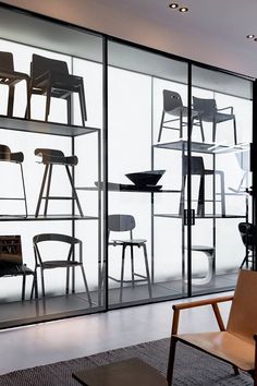 an empty chair in front of a glass wall with shelves and chairs on it's sides