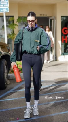 a woman walking down the street in tights and sports bra with an orange water bottle