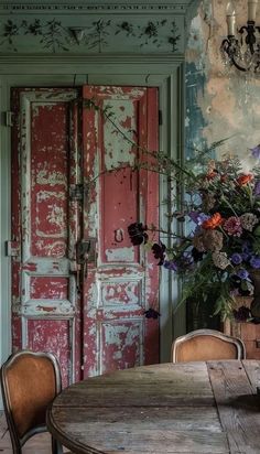 an old wooden table and chairs in front of a red door with flowers on it