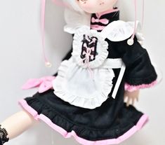 a doll with white hair wearing a black dress and pink ribbon around her neck is posed on a wall