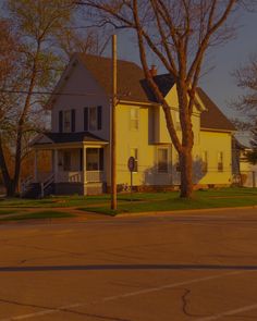 a yellow two story house sitting on the side of a road next to a tree