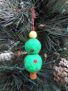 a green christmas ornament hanging from a pine tree