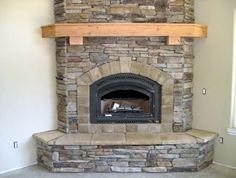 a stone fireplace in a living room with a wood mantel on top of it