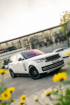 a white range rover parked in front of a building with yellow daisies around it