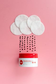 a red and white container with black dots coming out of it on a pink background