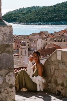 a woman sitting on top of a stone wall next to a body of water with buildings in the background