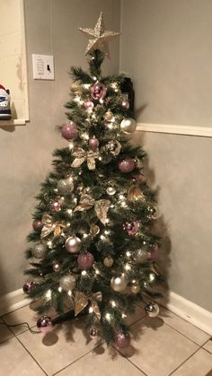 a small christmas tree with silver and pink ornaments on it in the corner of a room