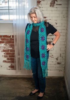 an older woman is standing in front of a brick wall and wearing a green scarf