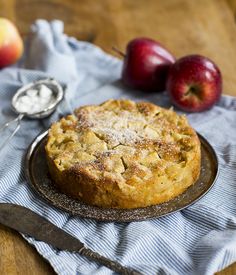 a pie sitting on top of a metal plate next to two apples and a spoon