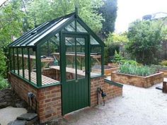 a small green house sitting on top of a brick wall next to a lush green forest