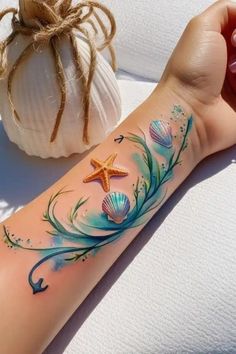 a person with a tattoo on their arm next to a seashell and starfish