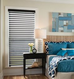 a bedroom with blue and white bedding in front of a window that has blinds on it