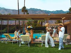 a group of people that are standing in the grass near some chairs and umbrellas