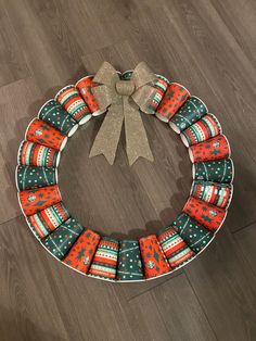 an orange and green christmas wreath sitting on top of a wooden floor next to a brown bow