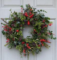 a christmas wreath hanging on the front door with holly, berries and pineconis