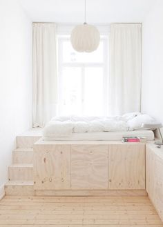 a bed sitting under a window in a bedroom next to a wooden floor and white walls