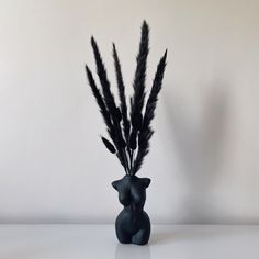 a black vase with feathers in it sitting on a table next to a white wall