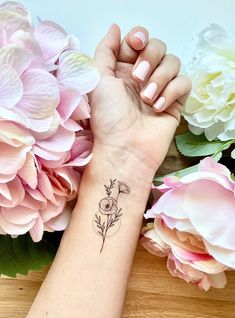 a woman's arm with a flower tattoo on it and flowers in the background