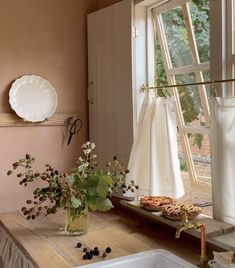 a kitchen counter with flowers and cookies on it next to an open window in front of the sink