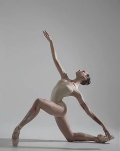 a woman in white leotard and ballet shoes doing a dance pose with her arms outstretched