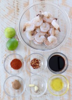 ingredients to make shrimp salad displayed in bowls on wooden table with limes and spices