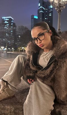 a woman wearing glasses sitting on the ground in front of a street light at night