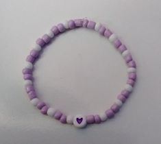 a purple and white beaded bracelet with a small heart charm on it's end