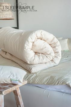 a bed with two pillows on top of it next to a table and lamp in the corner