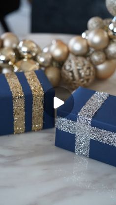 two wrapped presents sitting on top of a table next to christmas balls and ornaments in the background