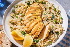 a white plate topped with chicken and rice next to slices of lemon wedged bread