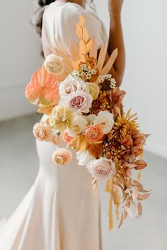 a woman holding a bouquet of flowers in her hand and wearing a white dress with an orange sash