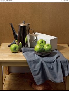 a wooden table topped with green apples next to a tea pot and silver kettle on top of it