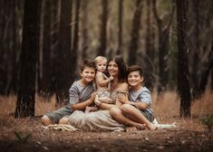 a woman and two boys are sitting on a blanket in the woods with their arms around each other